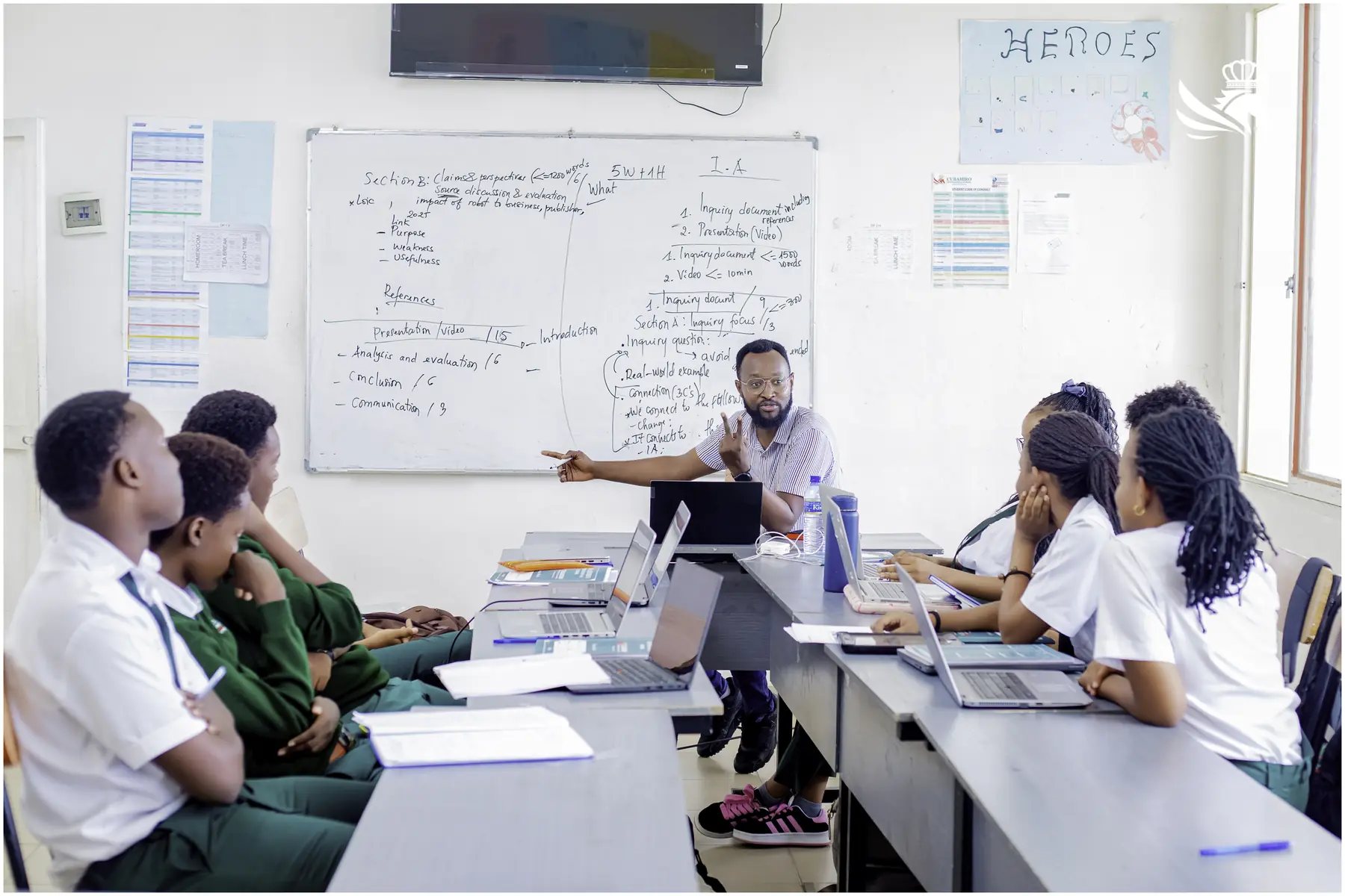 Teacher guiding students during a laptop-based lesson at Cubahiro International School